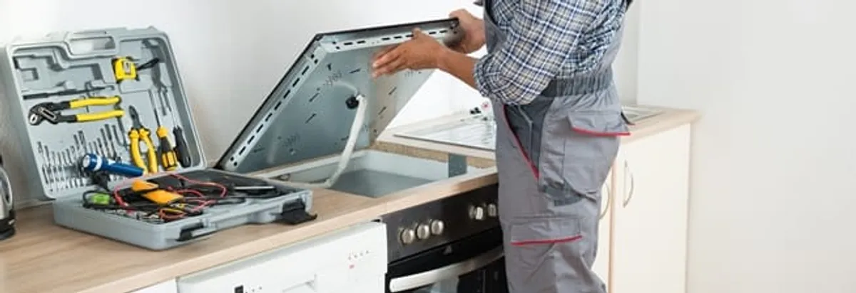 Cooktop repair technician lifting a built-in stovetop for service in Pittsburgh, PA