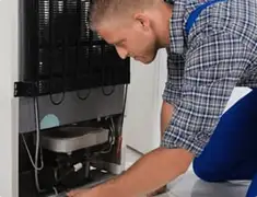 Refrigerator repair technician servicing the compressor and condenser area in Pittsburgh, PA